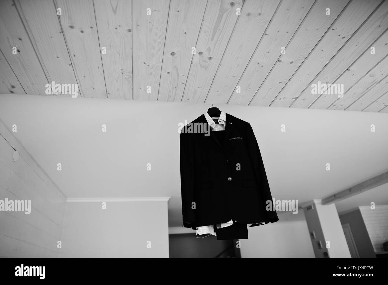 Groom's wedding suit hanging on the rack in big light room. Black and white photo. Stock Photo