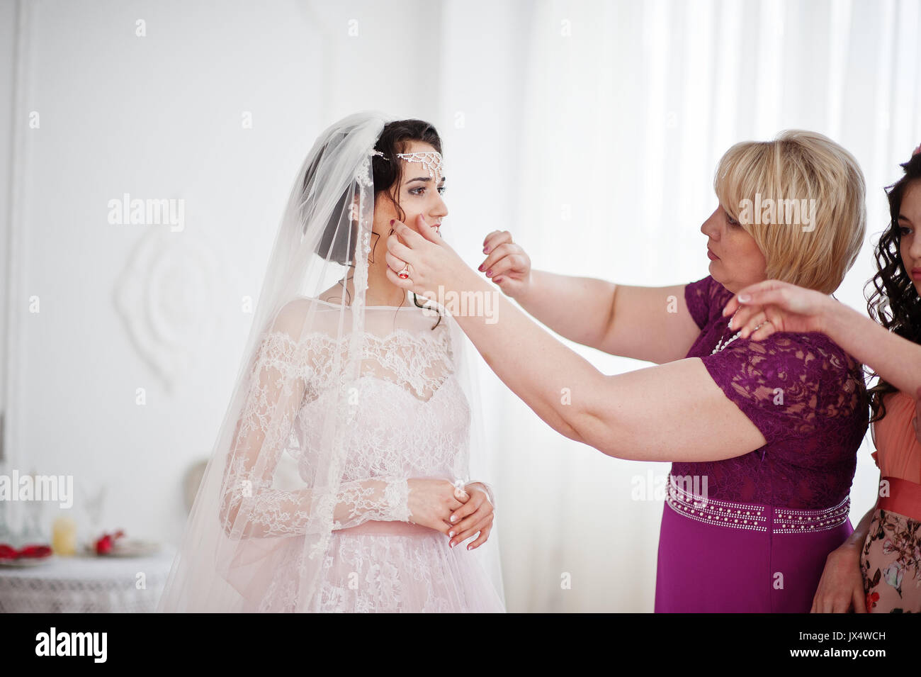 Bridesmaids and mother helping bride to dress up and get ready for her ...