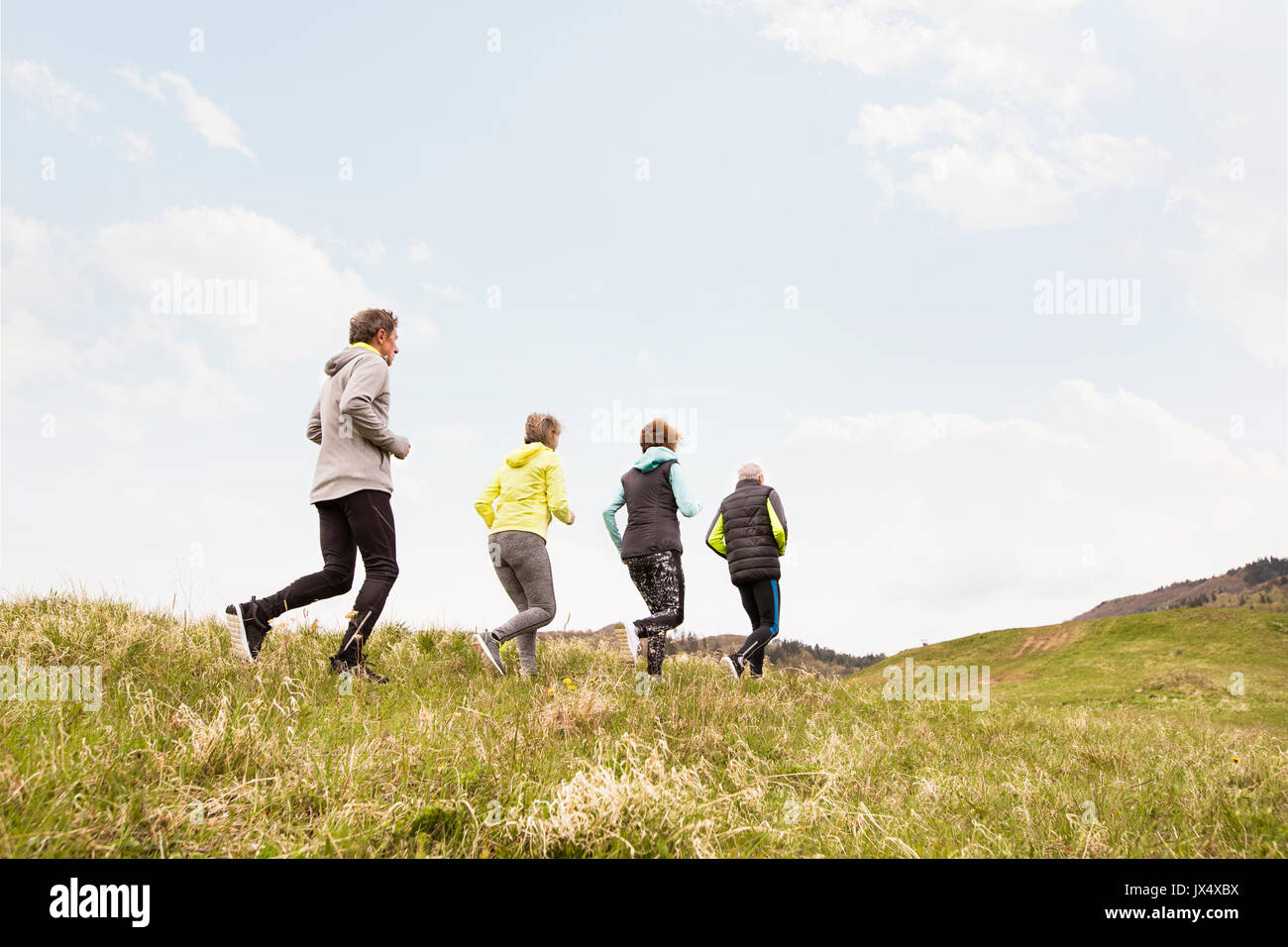 Group of active seniors running together outside on the green hills. Stock Photo