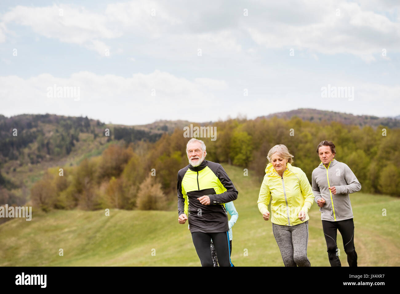 Group of active seniors running together outside on the green hills. Stock Photo