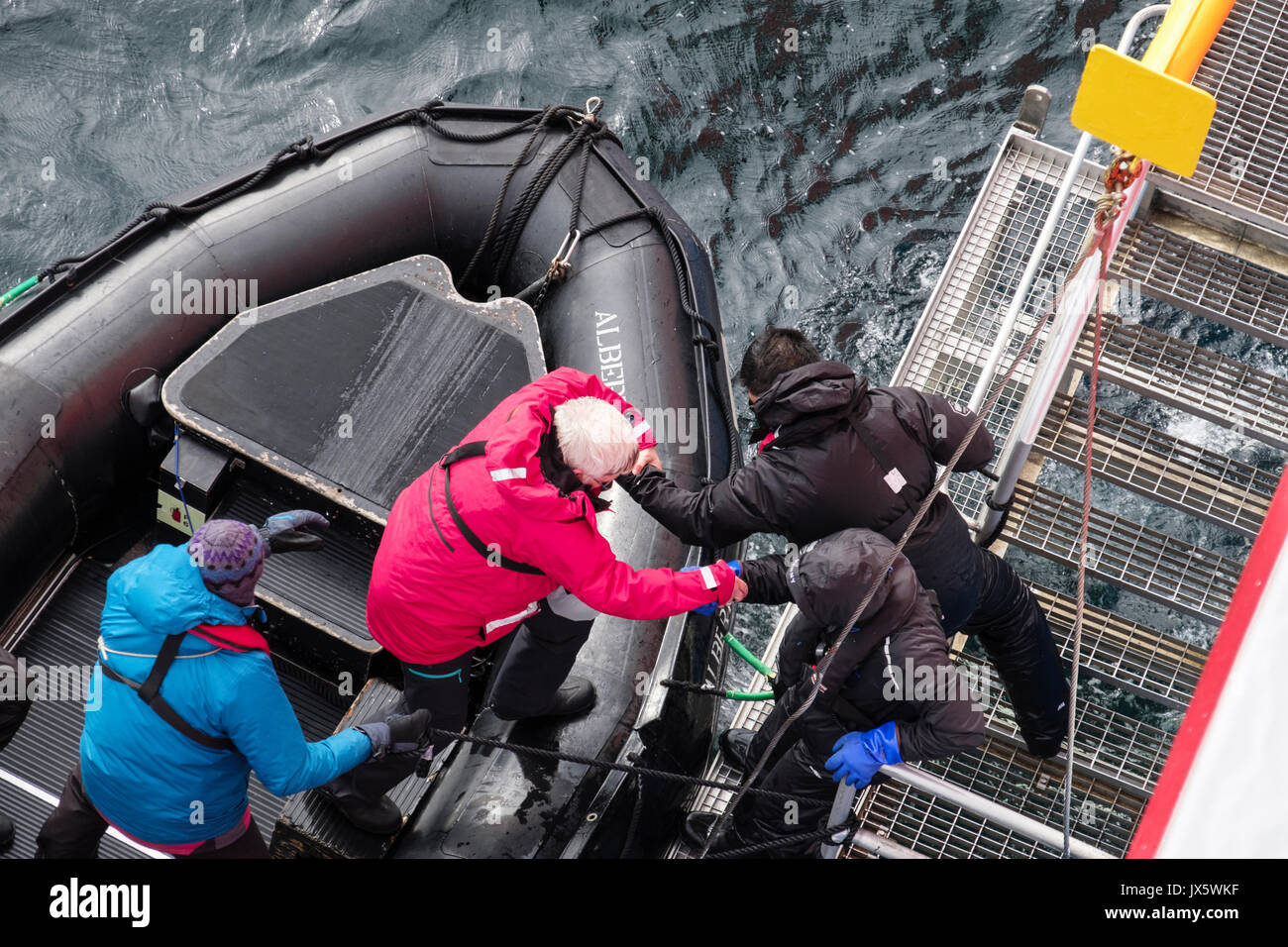 G Adventures Expedition cruise ship passenger being helped from a Zodiac dinghy back on board by crew using a sailors grip. Norway, Scandinavia Stock Photo
