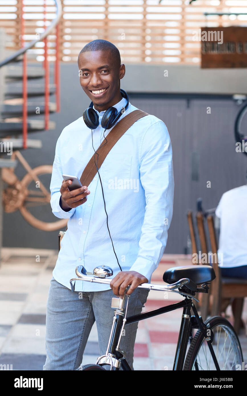 Smiling man standing with his bike using a cellphone Stock Photo
