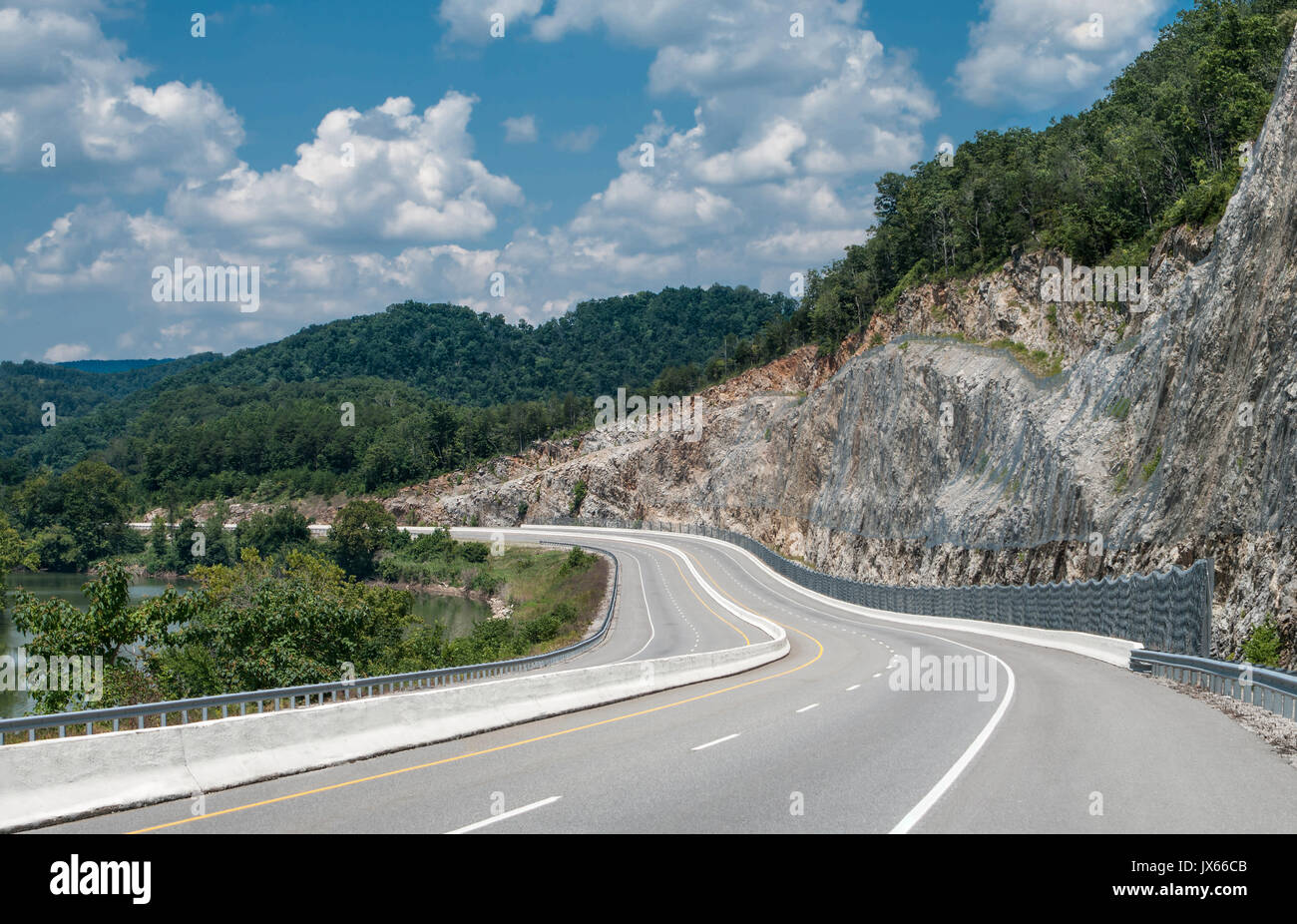 Appalachian Mountain Highway:  A four lane divided highway curves between a winding river and a steep cut rock face in eastern Tennessee. Stock Photo