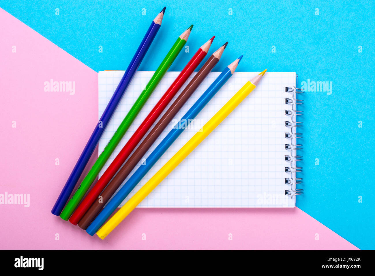 Notepad for notes and colorful pencils on colored background. Studio Photo Stock Photo