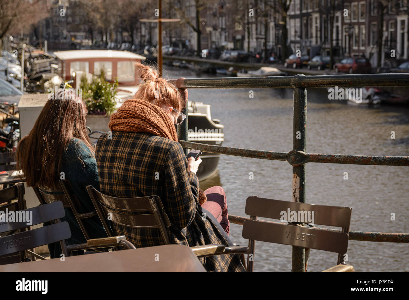 Young people reading books in an outdoor café along a canal in Amsterdam (Netherlands). March 2015. Portrait format. Stock Photo