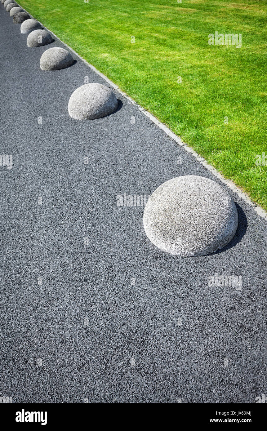 Abstract background made of asphalt floor, lawn and row of hemisphere barriers. Stock Photo
