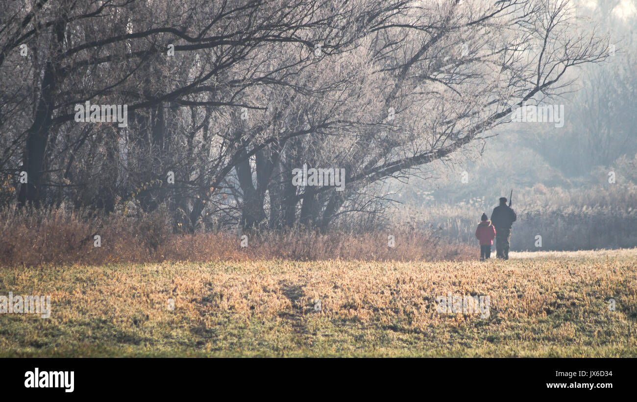 Panorama with two hunters at sunrise. Hunter man and boy during hunting period in search of wildfowl or game. Autumn hunting season. Grandfather teach Stock Photo