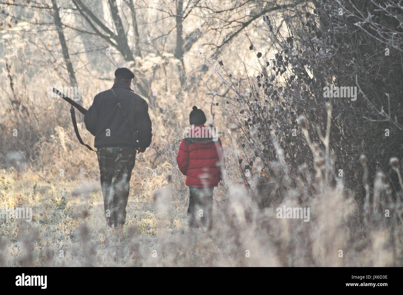 Two hunters at sunrise. Hunter man and boy during hunting period in search of wildfowl or game. Autumn hunting season. Grandfather teaches his grandso Stock Photo