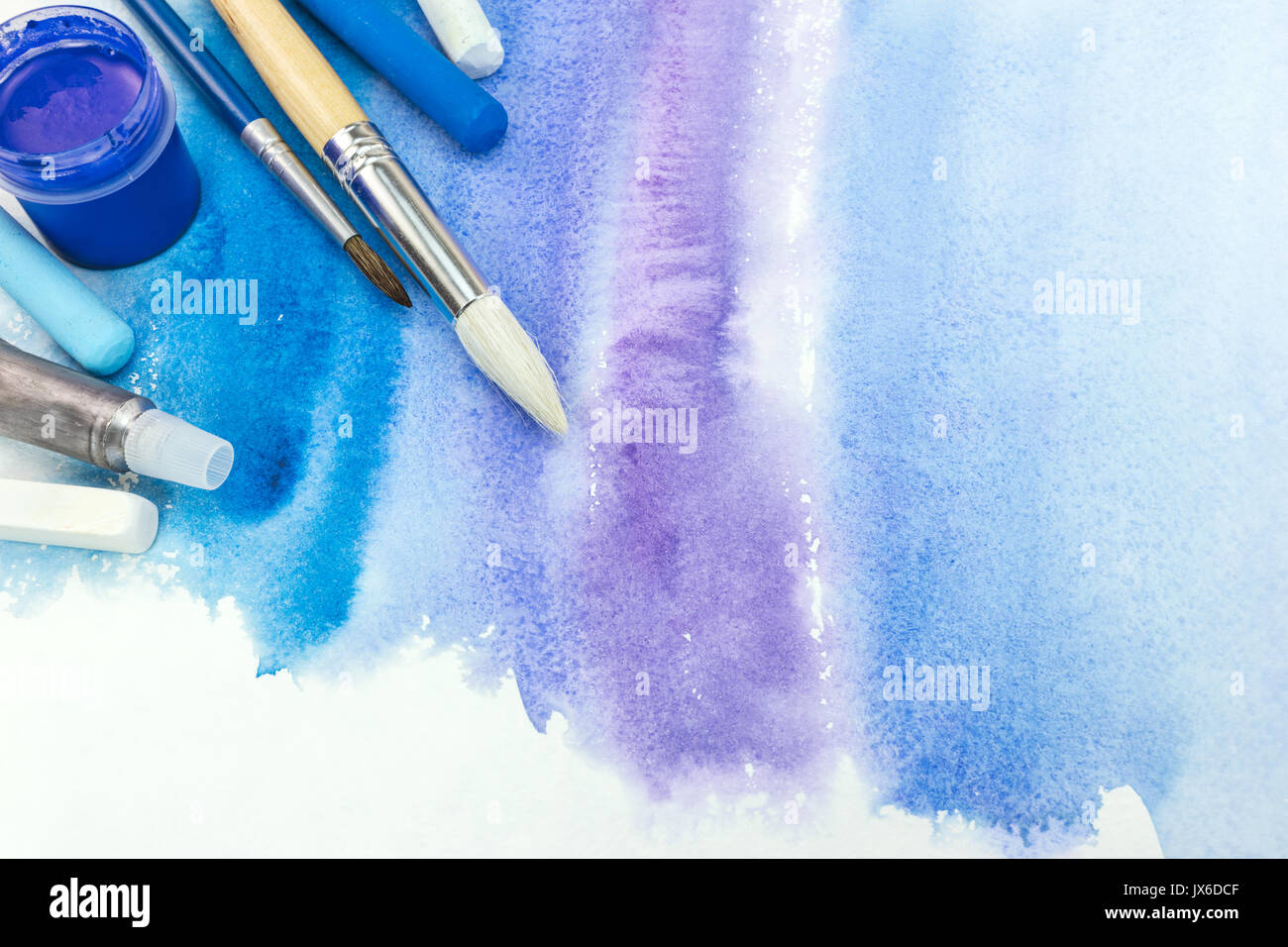 paintbrushes with paint and pastel crayons on blue watercolor