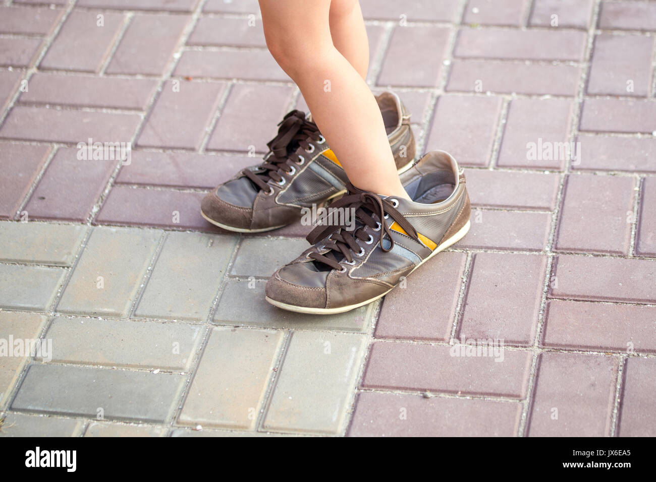 Little kid wearing large adult's old brown sneakers. Stock Photo