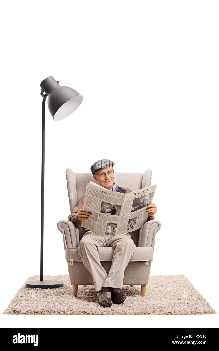 Elderly man reading a newspaper in an armchair next to a lamp isolated on white background Stock Photo