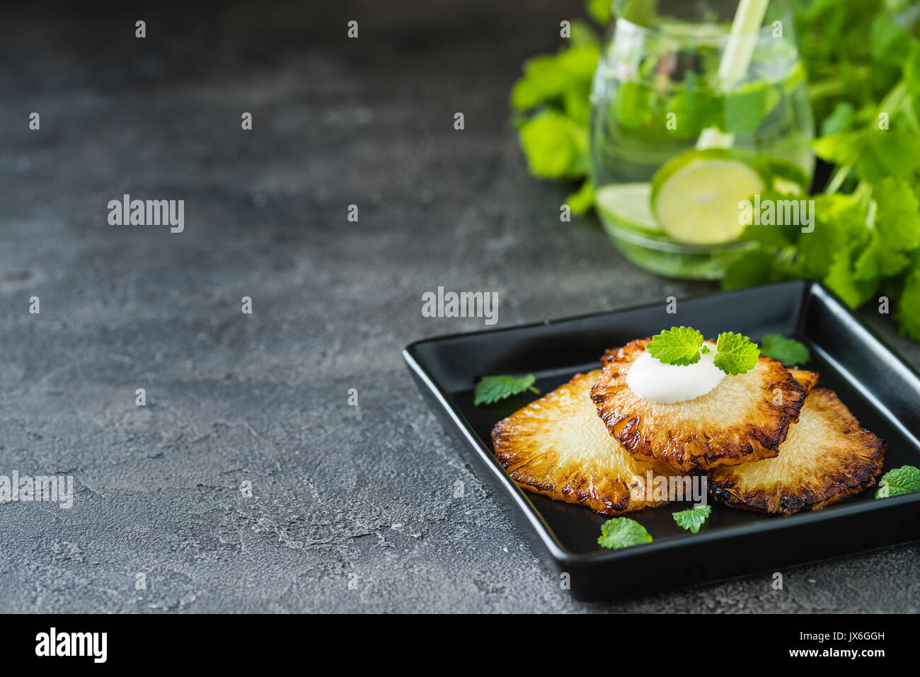 Fried pineapple slices with creme fraiche, mint on dark background. Copy space Stock Photo