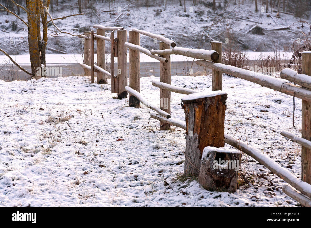 Rural nature seasonal scene: wooden fence in winter forest near a river covered by snow Stock Photo