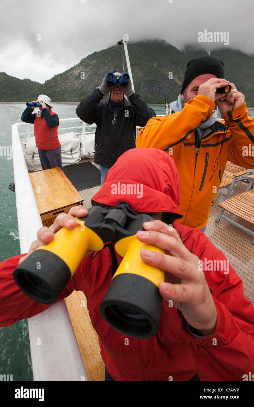 During an expedition on a cruise ship, passengers use binoculars to scan the landscape. Stock Photo