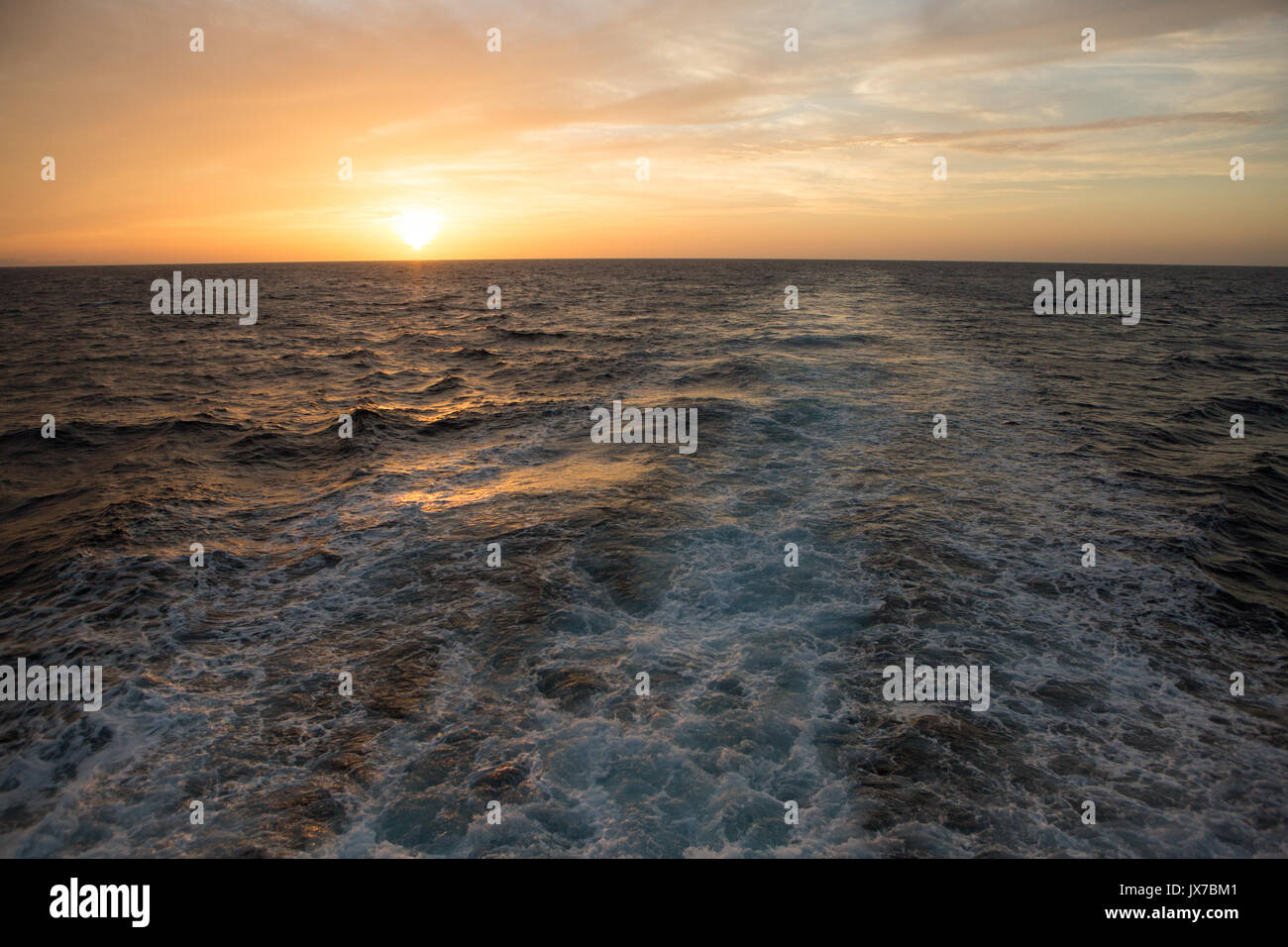 The sun rises above the horizon as waves and wake are visible  in waters near Isla Coiba National Park. Stock Photo