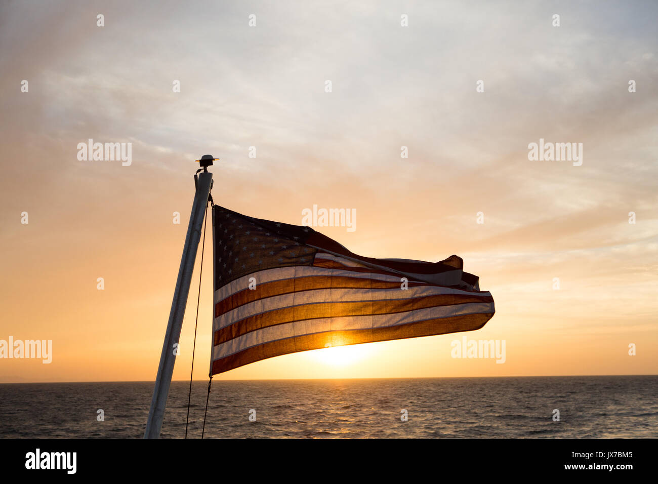 In waters near Isla Coiba National Park, the sun rises and illuminates an American flag that flies from an expedition cruise ship. Stock Photo