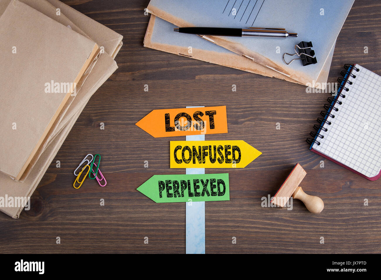 Lost, confused and perplexed concept. Paper signpost on a wooden desk. Stock Photo
