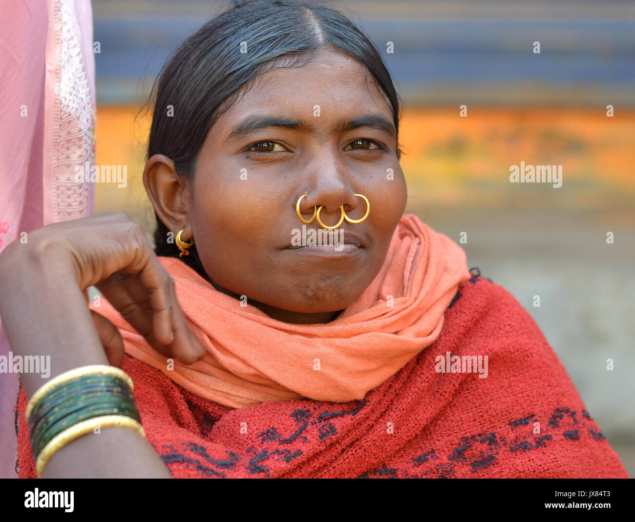Closeup street portrait (outdoor headshot, three-quarter view) of a young Indian Adivasi market woman with three golden tribal nose rings. Stock Photo