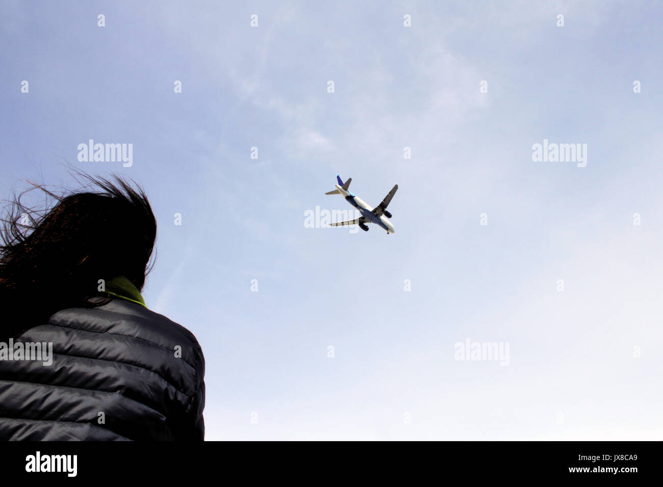 A young woman with dark hair looks up at an airplane as it comes in for a landing. Stock Photo