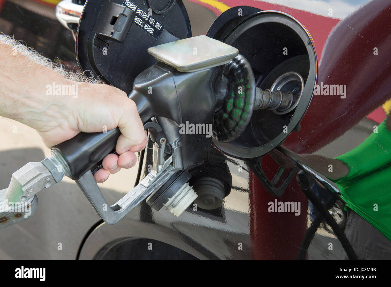 Hand of man holding gas station nozzle pumping fuel into black vehicle