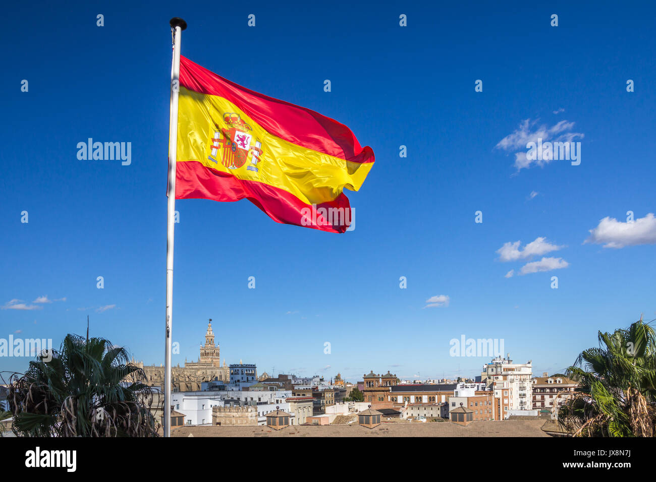 Spanish flag flies over Seville skyline including Cathedral at lower edge of frame.  Bright blue sky provides contrasting background and copy space. Stock Photo