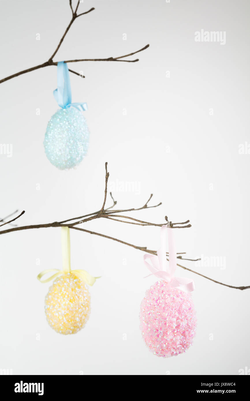 Three sequin encrusted Easter eggs hanging on branch with copy space. Stock Photo