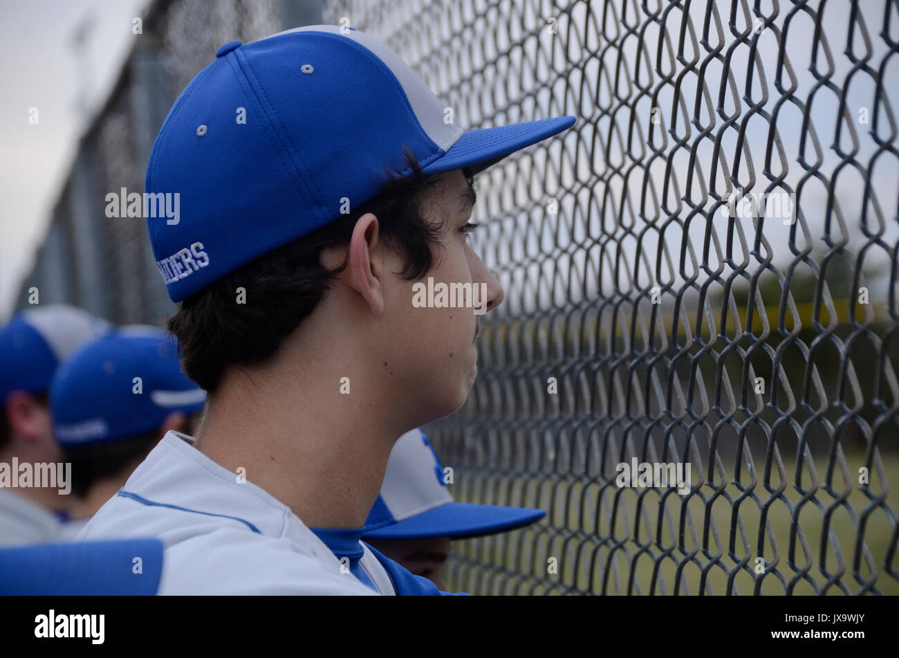 teen watching a baseball game through a fence Stock Photo