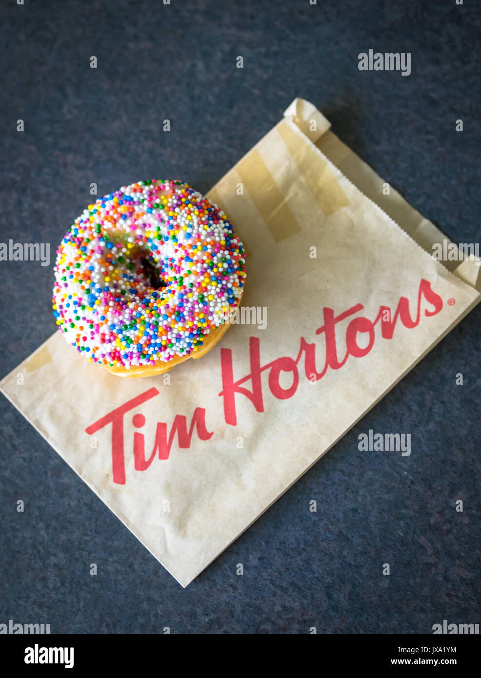 A vanilla dip donut (sprinkle donut, rainbow sprinkle donut) from Tim Hortons, a popular Canadian fast food restaurant and donut shop. Stock Photo