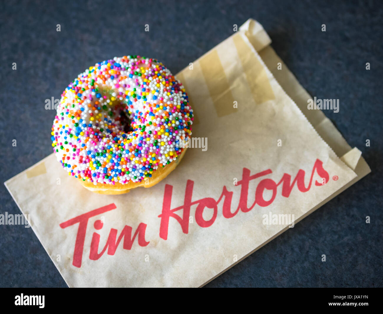 A vanilla dip donut (sprinkle donut, rainbow sprinkle donut) from Tim Hortons, a popular Canadian fast food restaurant and donut shop. Stock Photo