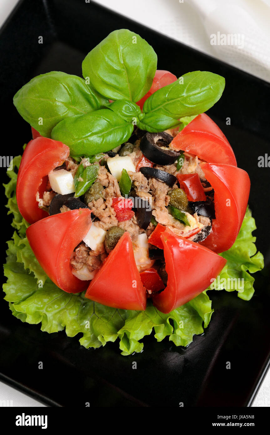 Festive appetizer. Tomato stuffed with chopped tuna salad, egg, tomato cubes, olive slices and the addition of capers, greens Stock Photo