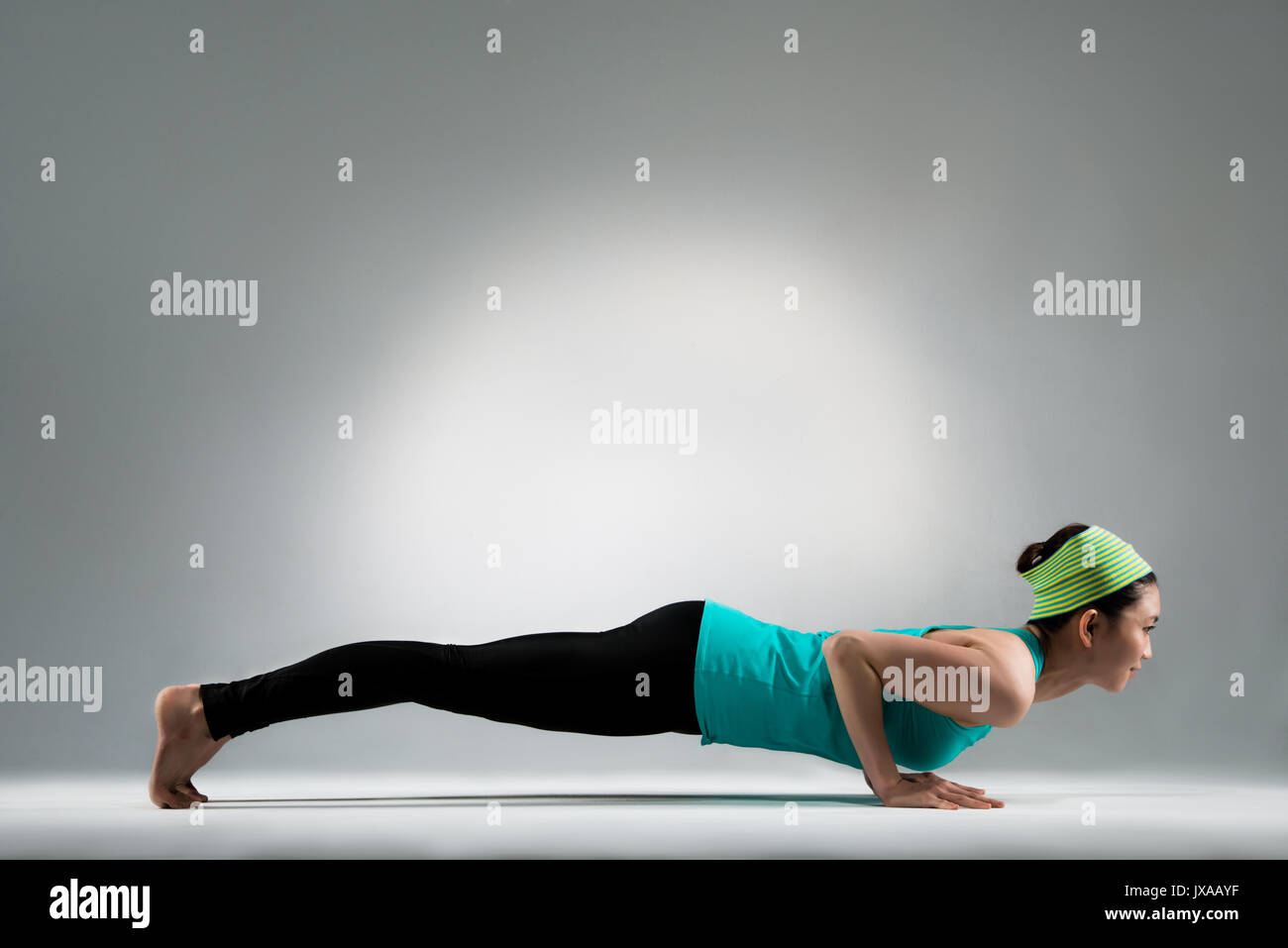 smiling gymnastic female player lying on ground floor hands up body performing pushup posture at yoga fitness center studio with gray wall background. Stock Photo