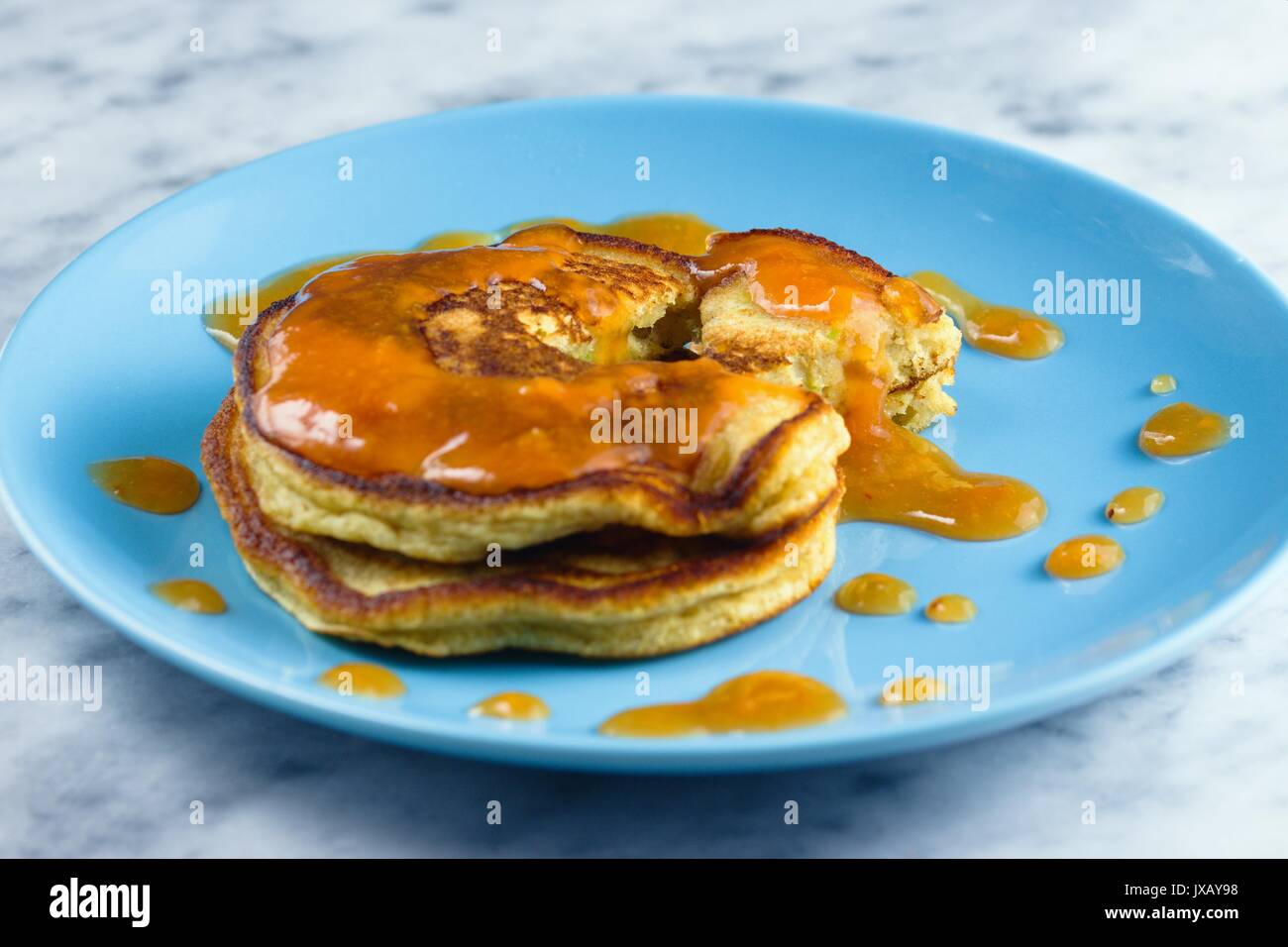 Two crumpets from gluten free flour with peach preserve on blue plate Stock Photo