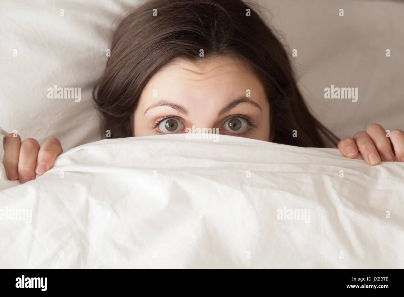 Funny surprised girl covering face with white blanket, headshot  Stock Photo