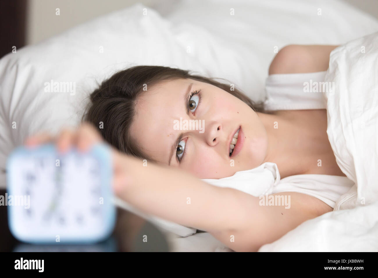 Annoyed sleepy young woman turns off alarm clock, bad wakeup Stock Photo