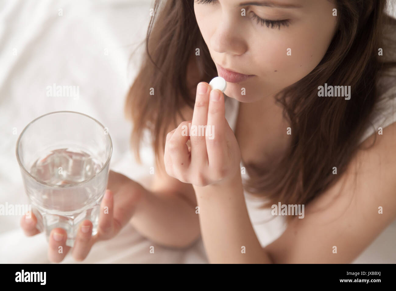 Unhealthy sick young woman taking sleeping pill sitting in bed Stock Photo