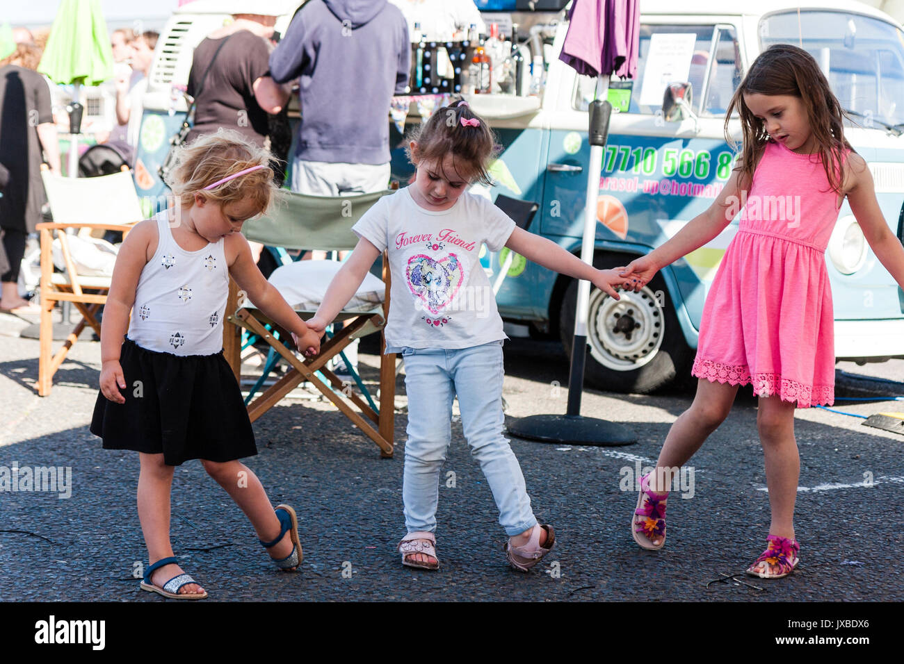 Three young Caucasian children, girls, 5-6 years old, dancing outdoors holding hands in a row. Stock Photo