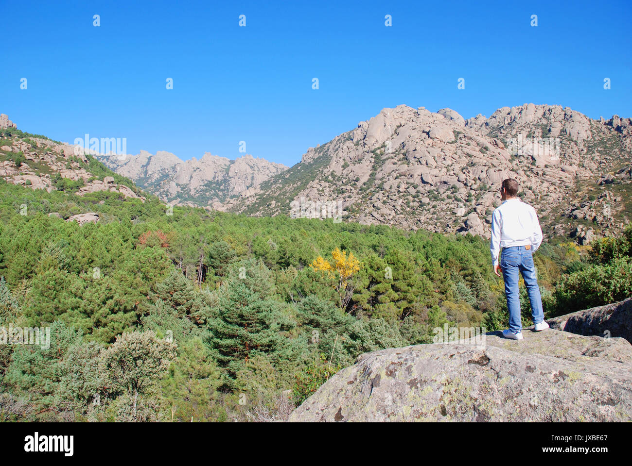 Man standing on a stone, watching the landscape. Parque Regional de la Pedriza de Manzanares, Manzanares El Real, Madrid province, Spain. Stock Photo