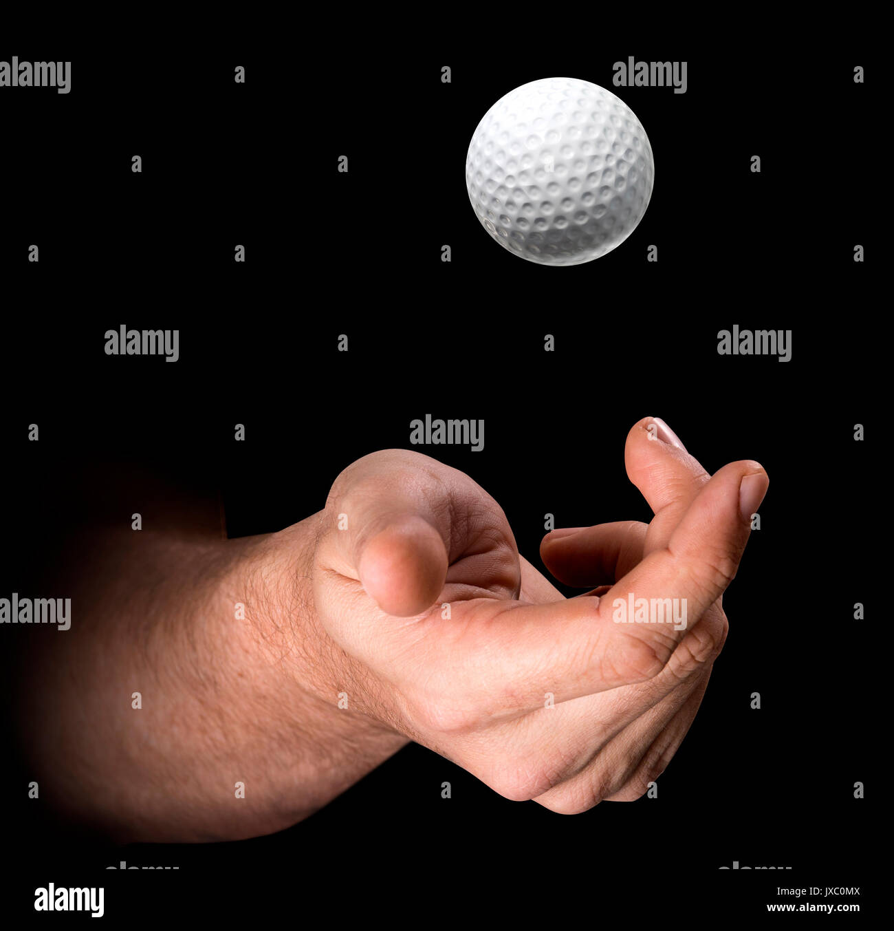 A male hand tossing a golf ball up in the air on an isolated dark ...