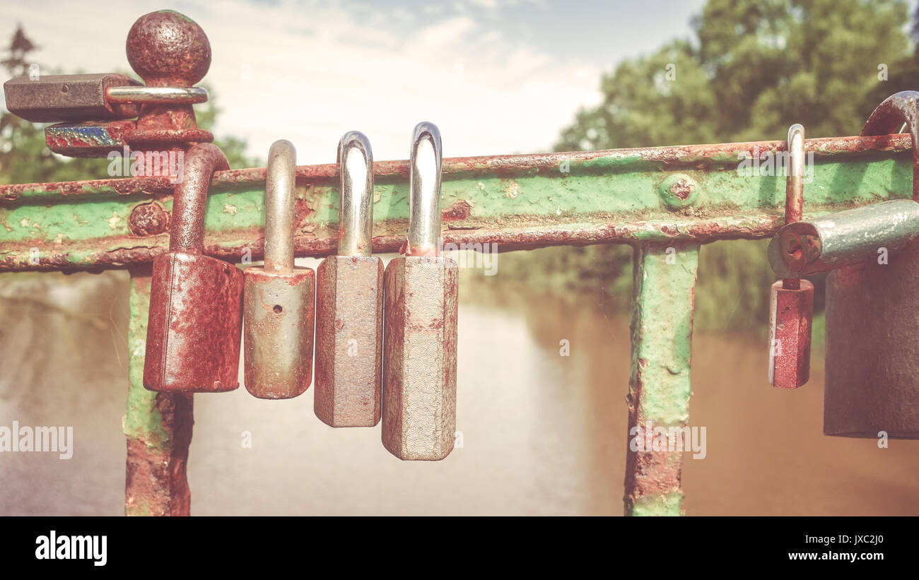 Retro stylized picture of old rusty padlocks on a bridge, love symbol, shallow depth of field. Stock Photo