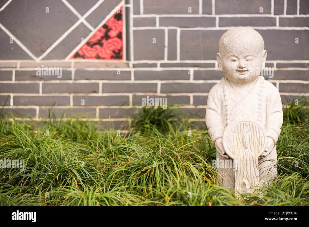 Little buddha stone statue on grass with a brick wall in the bac Stock Photo