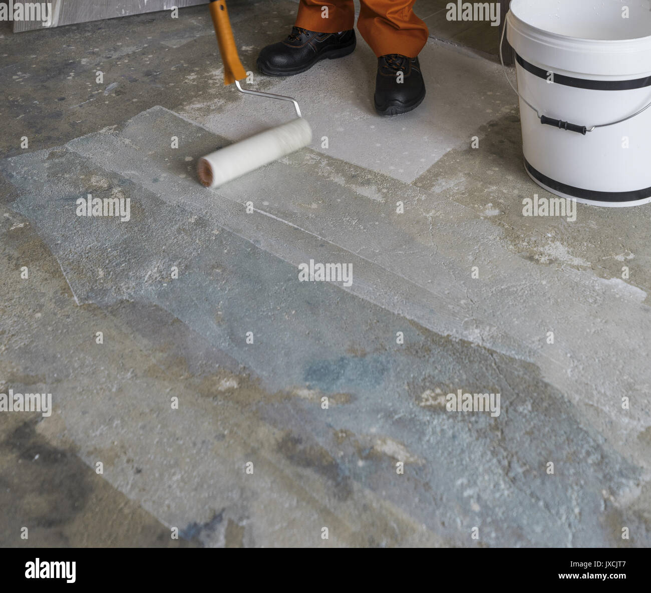 Renovation of house. Worker puts primer with roller on concrete floor Stock Photo
