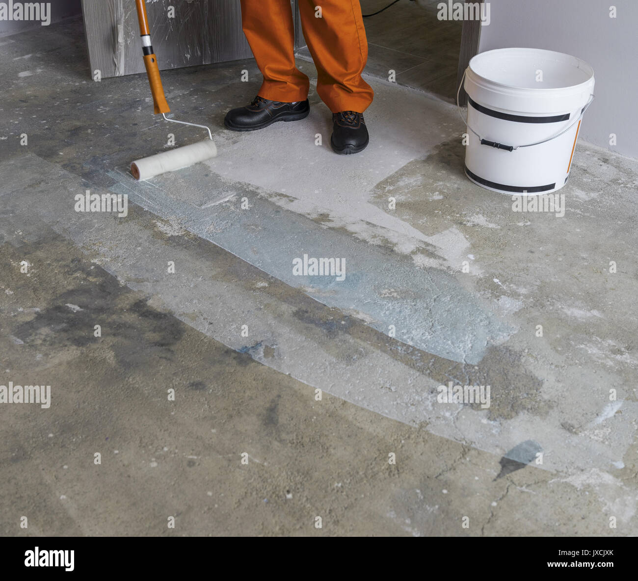 Renovation of partment. Worker puts primer with roller on concrete floor Stock Photo
