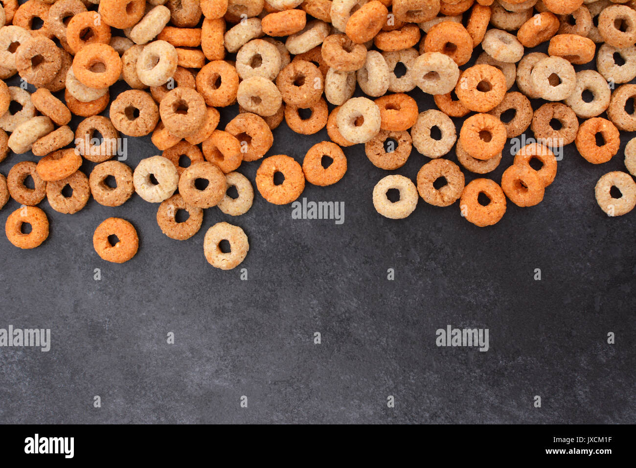 Multigrain hoops breakfast cereal border with copy space on a dark grey slate tile background Stock Photo