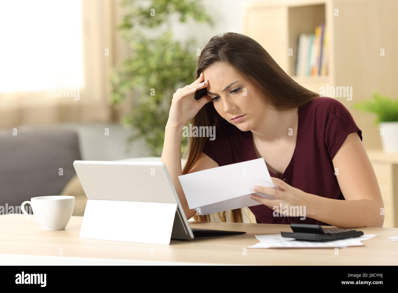 Worried woman calculating accountancy reading a letter sitting in a desk at home Stock Photo