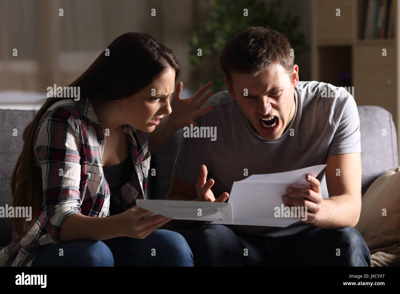 Furious couple reading a letter sitting on a couch at home Stock Photo