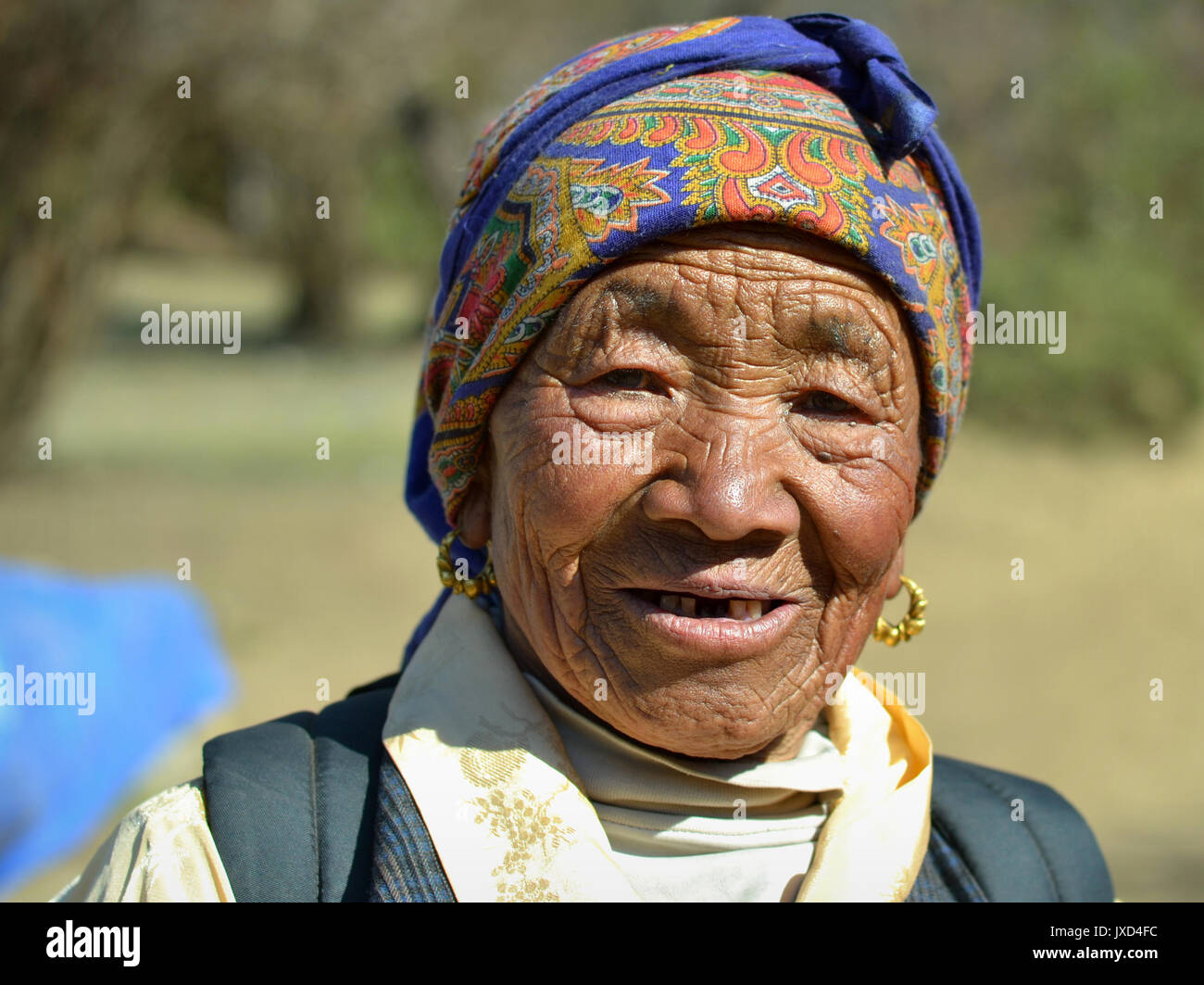 Old Sherpa woman with live-in face and traditional golden earrings poses for the camera. Stock Photo