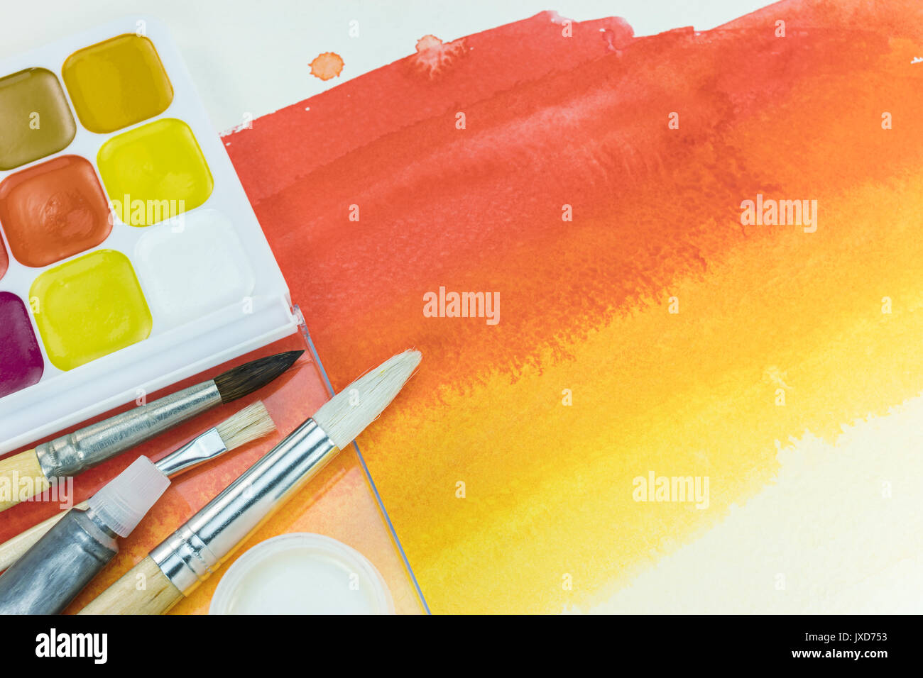 palette of watercolor paints and various paintbrushes on red yellow ...