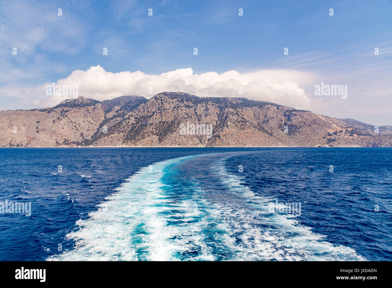 Wake on the surface of a sea and hilly island in the background, landscape Stock Photo
