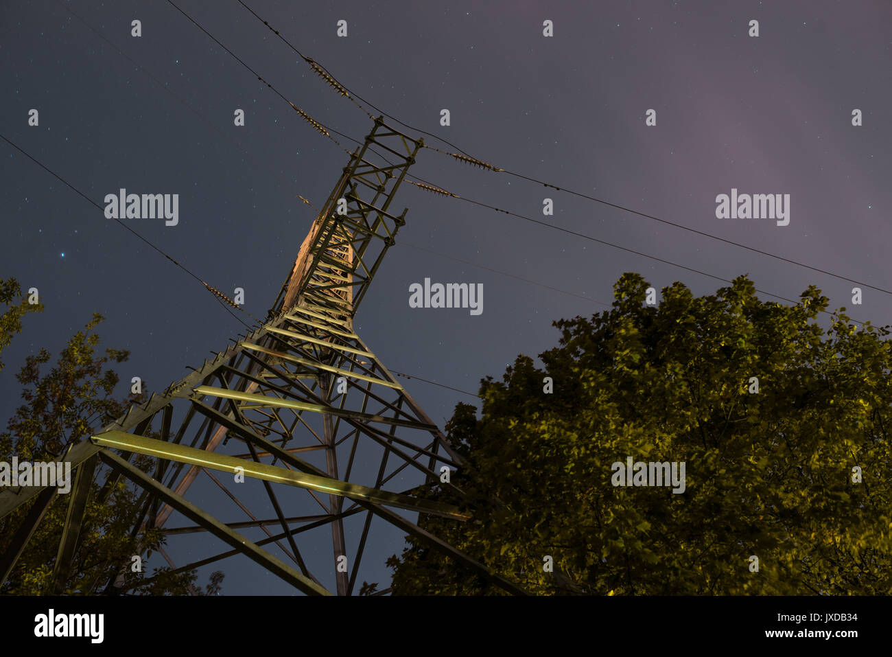 High voltage post or tower up view with tree and night sky clouds. Long exposure photography Stock Photo