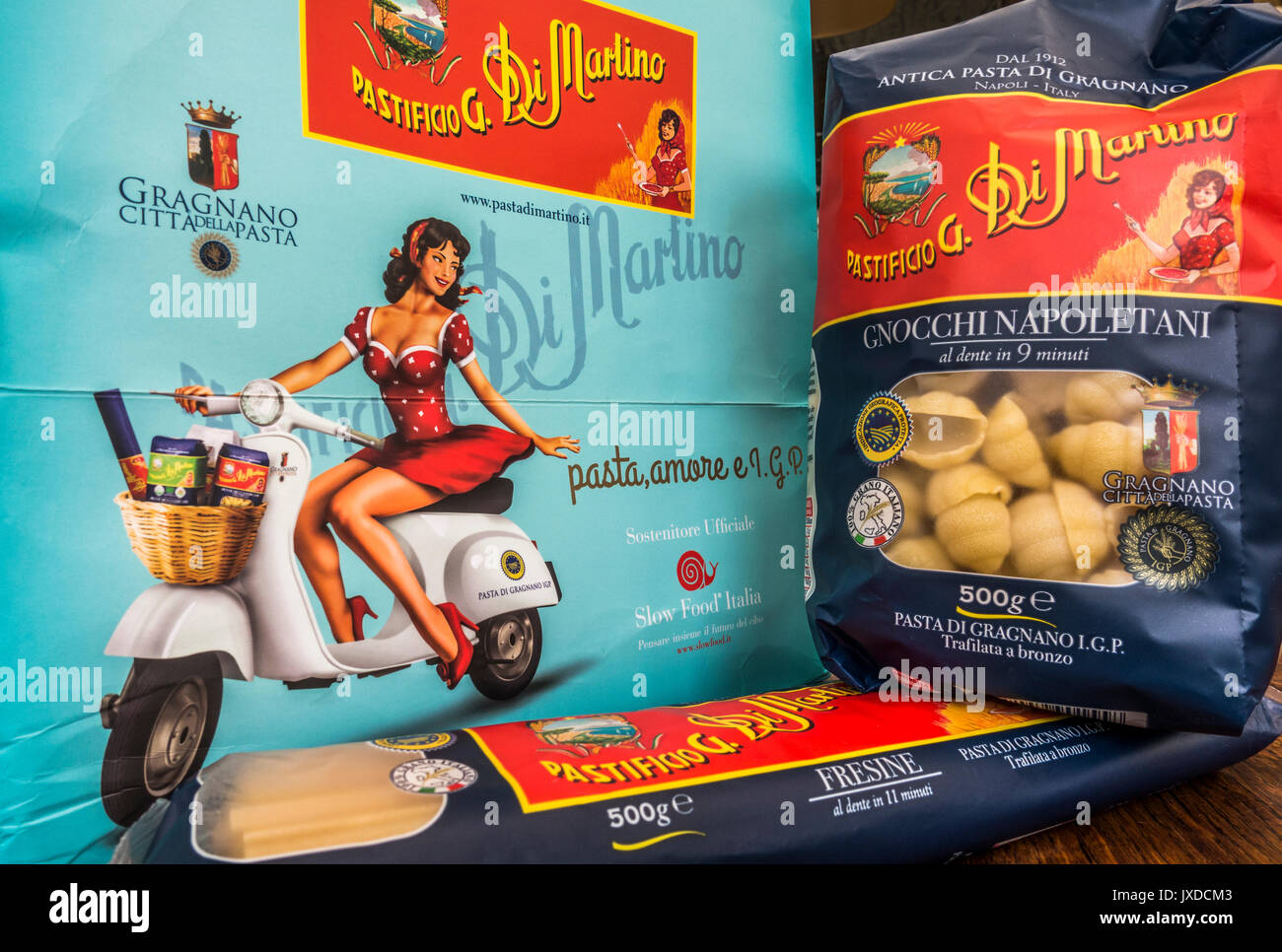 Combined Pasta di Martino products - dry spaghetti and shells in separate packs, against a presentation box showing a girl on an Italian make scooter. Stock Photo